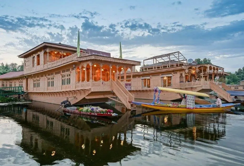 Scenic houseboat on tranquil waters of Kashmir, framed by majestic mountains and vibrant flora."